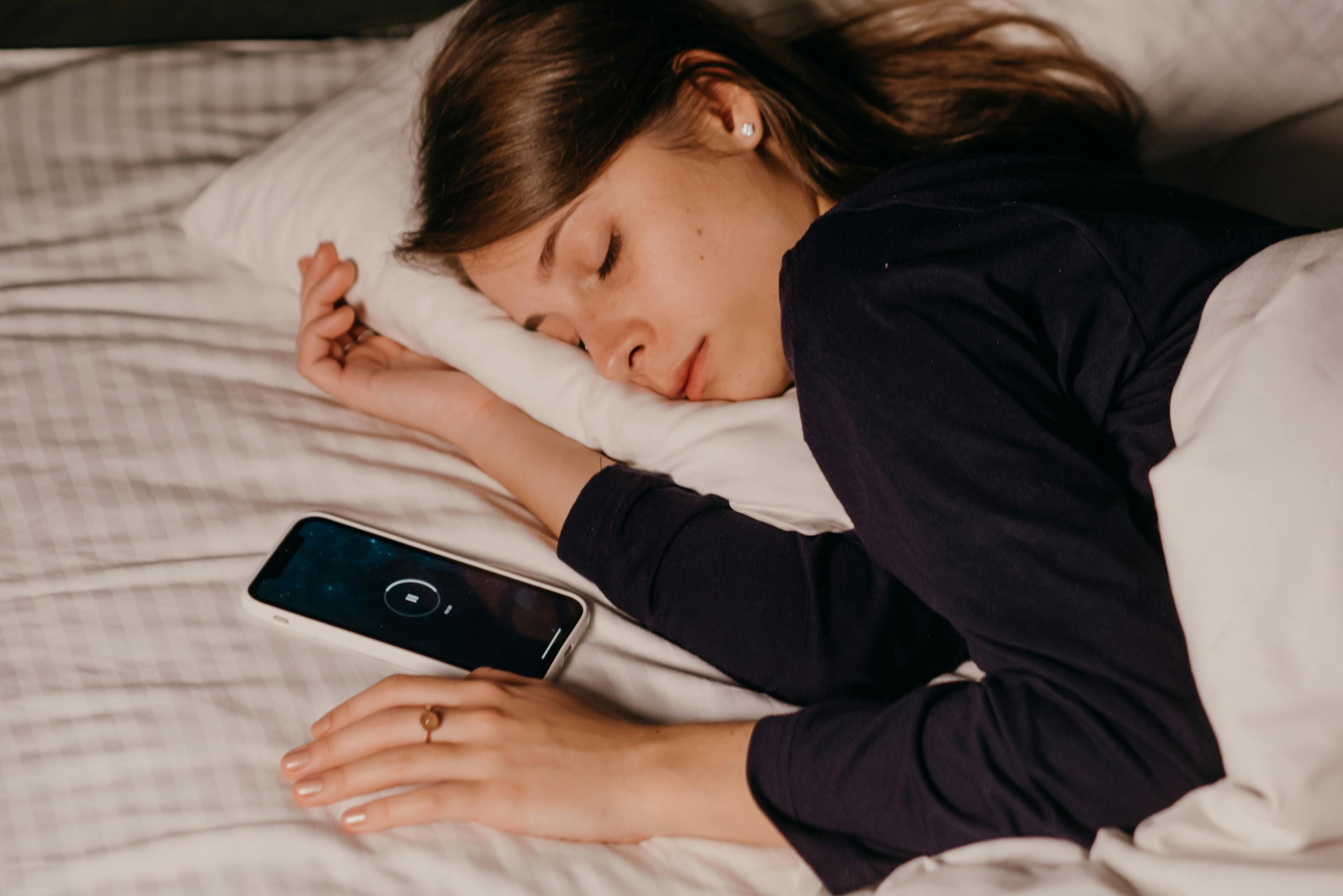 Person sleeping beside a smartphone playing ambient sound, illustrating the role of sound in sleep and white noise environments