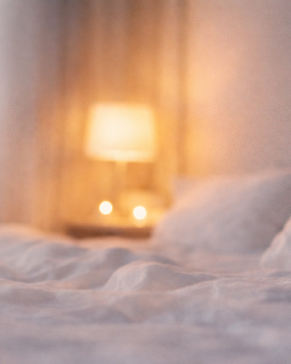 Softly lit bedroom with rumpled white bedding and a warm bedside lamp, creating a calm sleep environment.