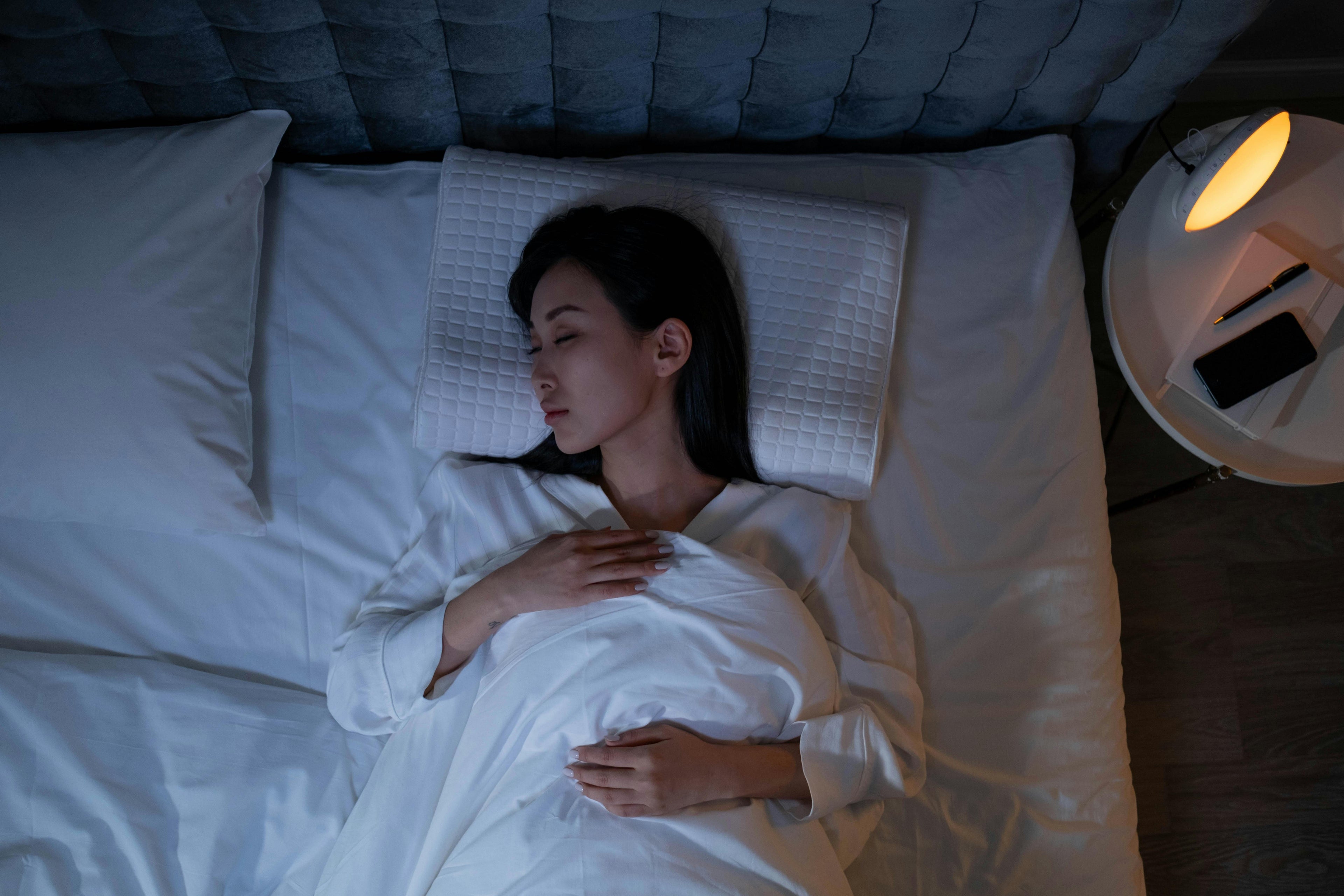 Woman sleeping peacefully in a calm, dimly lit bedroom environment, illustrating listening to audio while sleeping